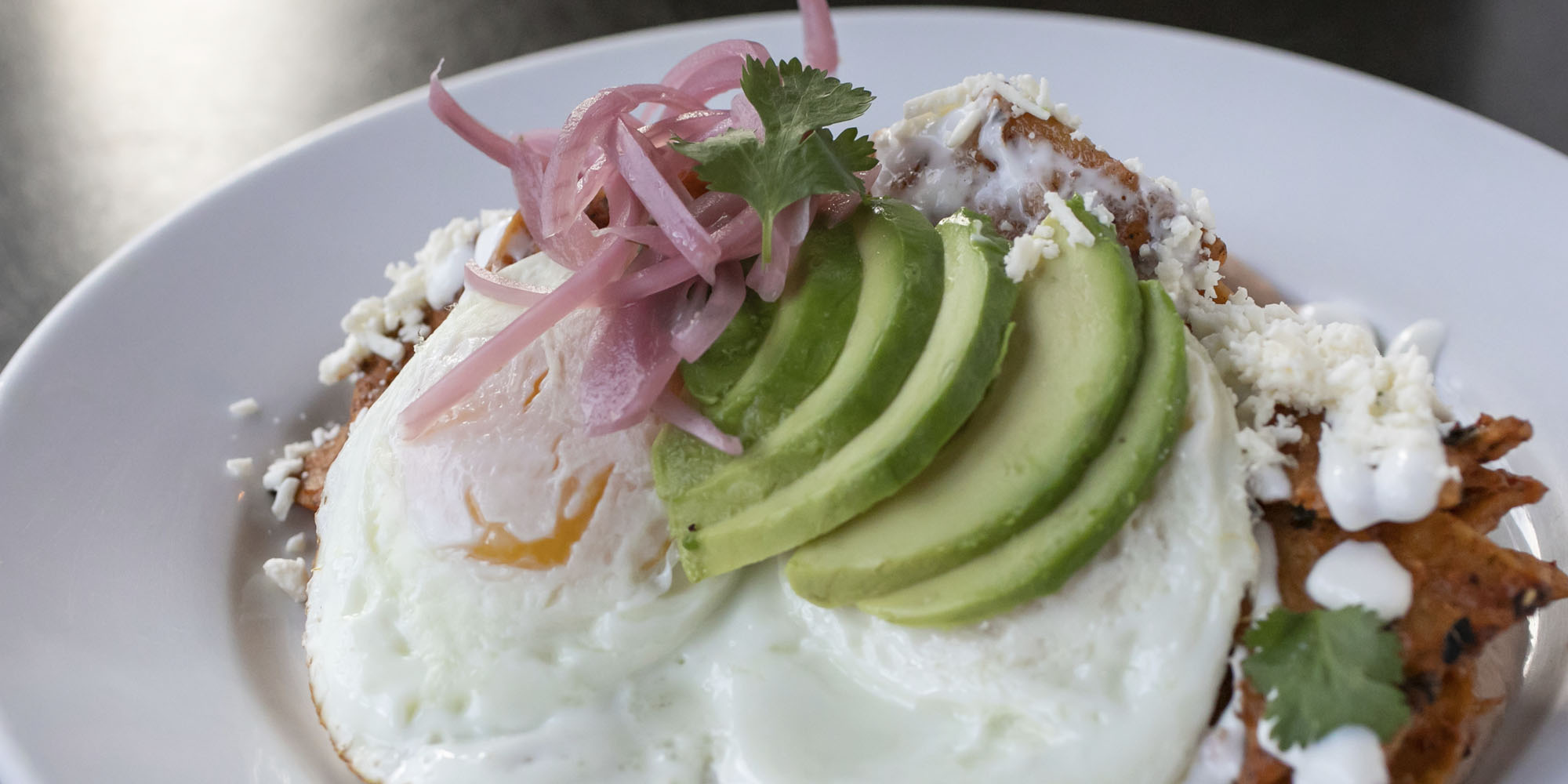 Photo of a plate of chilaquiles with eggs and avocado on top